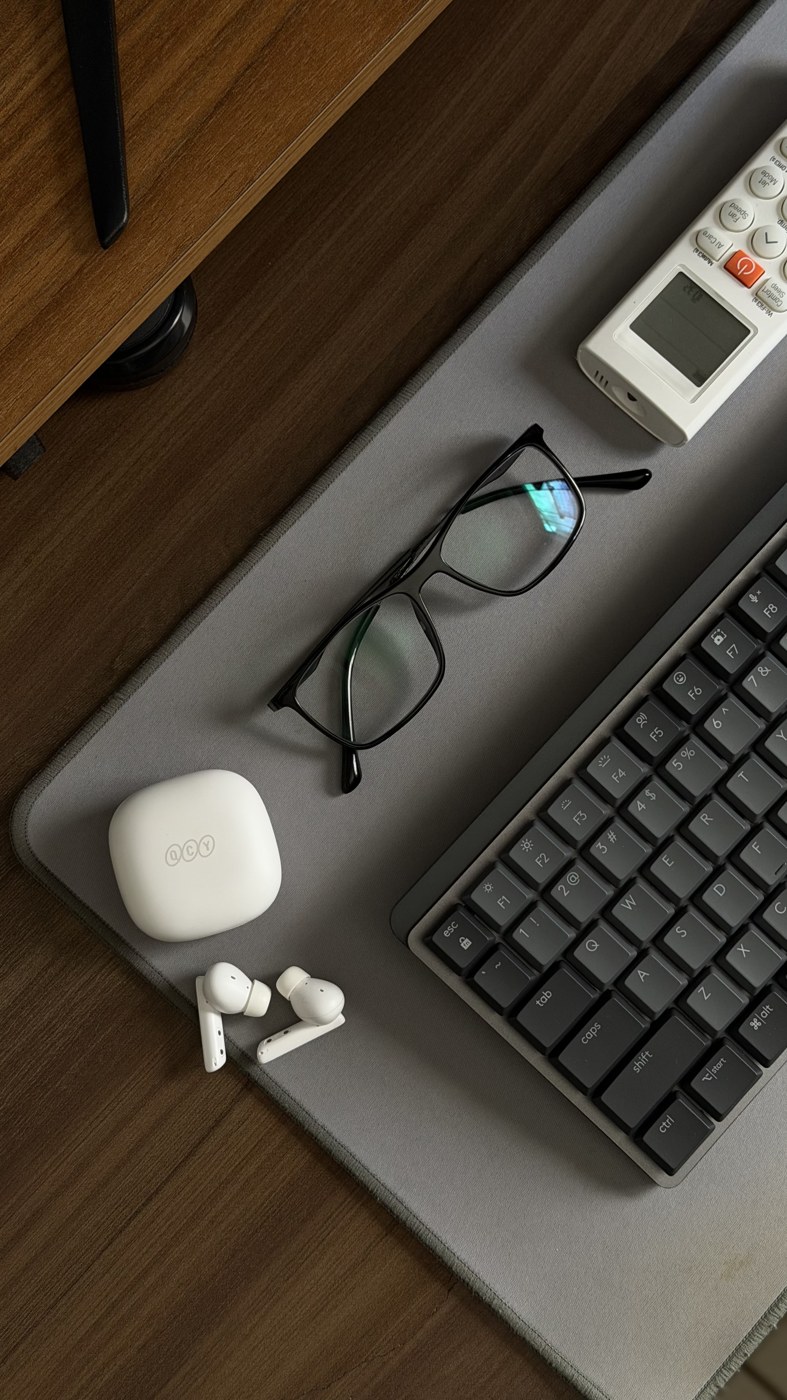 Mesa de trabalho vista de cima: óculos, fones, teclado